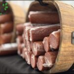 A wooden bucket filled with sausages sits on a table.