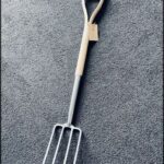 A wooden handle with a metal head sits on a grey carpet.