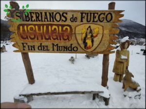 A wooden sign that says "Ushuaia fin del mundo" is covered in snow.