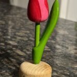 A wooden vase with a pink flower in it.