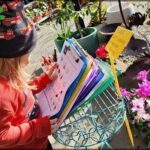 A young child is holding a clipboard with papers on it, possibly learning about plants.