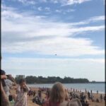 A young girl is pointing at a plane flying in the sky, while a crowd of people watches the spectacle.