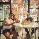 Three people are sitting at a table, enjoying drinks and each other's company.