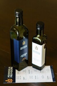 Two bottles of olive oil sit on a table, one of which is labeled "Peninsula Provedore."