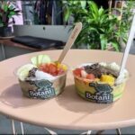 Two bowls of food are placed on a table, with spoons in them.