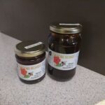 Two jars of honey sit on a counter, one with a red flower label and the other with a yellow label.