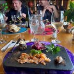 Two men are sitting at a table with wine glasses and plates of food.