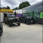 Two old military jeeps are parked in front of a building.