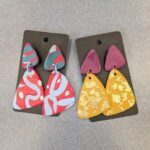 Two pairs of colorful earrings are displayed on a table.