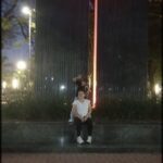 Two people sit on a bench in front of a large, illuminated sculpture.