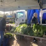 Two women are standing in front of a table filled with vegetables.