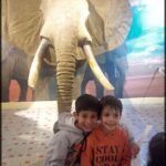 Two young boys pose for a picture in front of a large elephant statue.