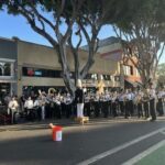 A band is playing in the street, with a man standing on a bucket.