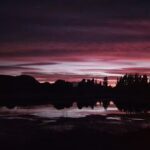 A beautiful sunset over a lake with trees in the background.