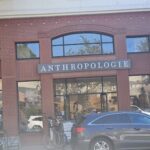 A black car is parked in front of a store called Anthropologie.