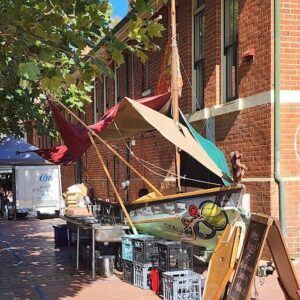 A boat is parked outside a building, and it appears to be a restaurant. The boat is covered with a canopy, and there are several people around the area.