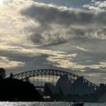 A boat is sailing in front of the Sydney Opera House, with the bridge in the background.