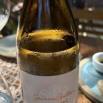 A bottle of wine is sitting on a table with a bowl of food.