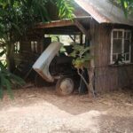 A broken down car is parked in front of a small shed.