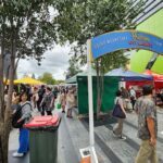 A bustling city market scene with people walking around and shopping.