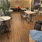 A caption for the image could be: "A wooden deck with a variety of chairs and tables, perfect for outdoor dining or relaxing."