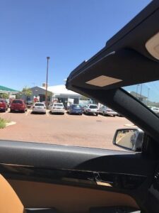 A car's rear view mirror captures a parking lot filled with various vehicles.