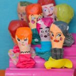 A collection of wooden figurines, each with a unique face, are displayed on a pink shelf.