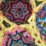 A colorful crocheted star with a blue center and orange and yellow edges.