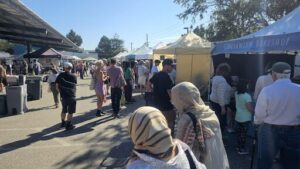 A crowd of people are gathered in a street market, with many of them wearing headscarves.