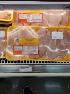 A display of raw chicken with a yellow container and a label.