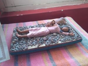 A doll is laying on a rocky surface, surrounded by rocks and a blanket.