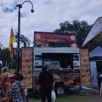 A food truck selling German sausages and currywurst is parked in a field.