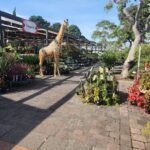 A giraffe statue stands in front of a flower shop, surrounded by various potted plants.