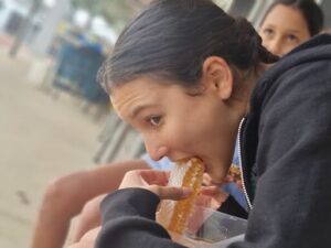 A girl is eating a piece of food, possibly a donut, while sitting down.