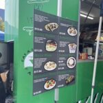 A green food truck with a menu board that says "Eat the Farm."