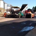 A group of men are working on a road, with a truck and a tractor nearby.