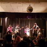 A group of musicians playing instruments on stage, with a crowd of people watching and enjoying the performance.