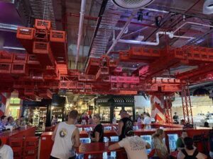 A group of people are gathered in a large room with a red ceiling, possibly a restaurant or a bar.