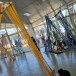 A group of people are gathered in a room with a variety of colorful objects, including a large number of strings and a few hammocks.