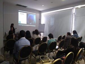 A group of people are sitting in a room, watching a presentation on a projector screen.