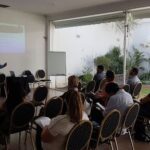 A group of people are sitting in chairs, attentively listening to a presentation.