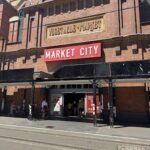 A group of people are walking into a building with a large red sign that reads Market City.