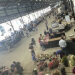 A large group of people are gathered in a building, possibly a market or a flower shop, with many potted plants and flowers on display.