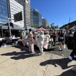 A large group of people are gathered in a city square, shopping and socializing.