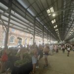 A large group of people are gathered in a marketplace, shopping for fresh produce.