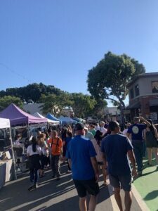 A large group of people are walking down a street, passing by tents and a building.