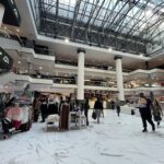 A large group of people walking through a mall, with some carrying backpacks and handbags.