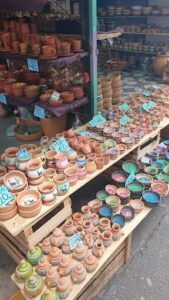 A large variety of pottery is displayed on a wooden table, including vases, bowls, and cups.