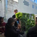 A man holds a leafy green plant in front of a group of people, capturing their attention.