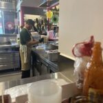 A man in a green shirt is preparing food in a restaurant kitchen.